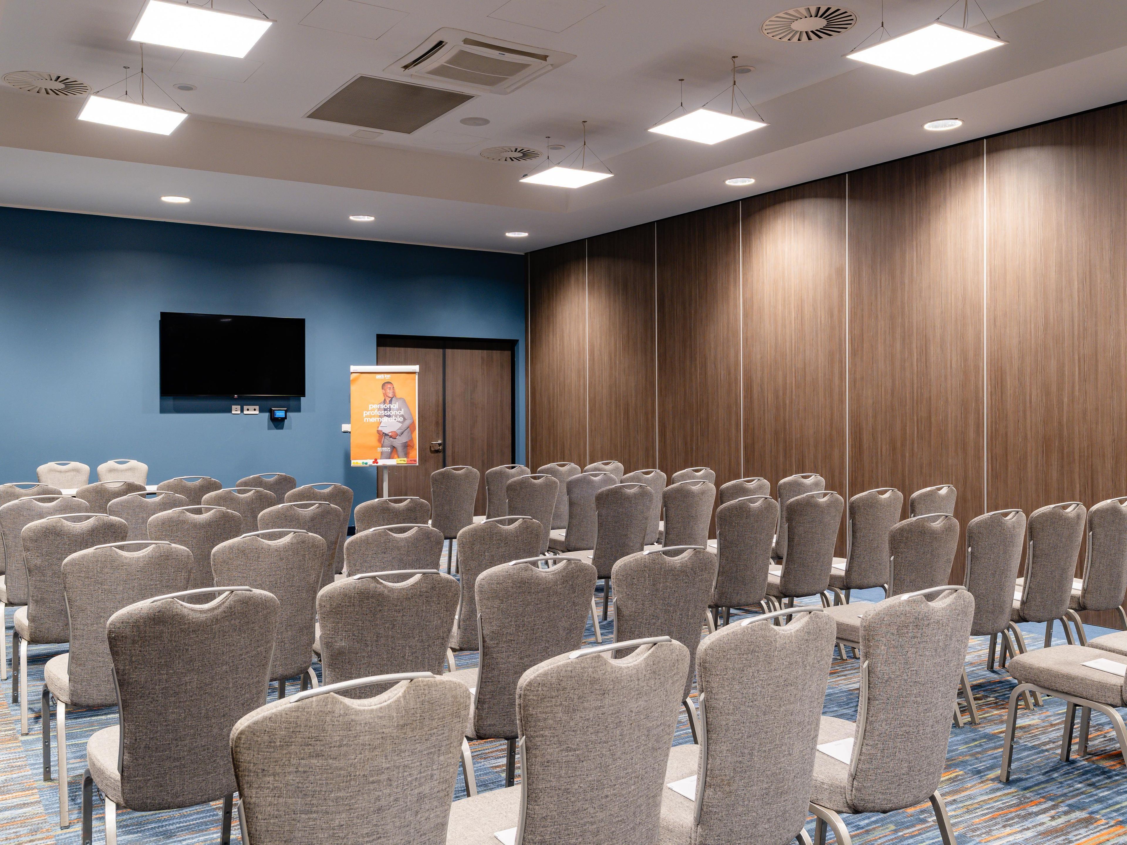Un salón de conferencias con filas de sillas, un televisor de pantalla plana en la pared y un revestimiento de paneles de madera.