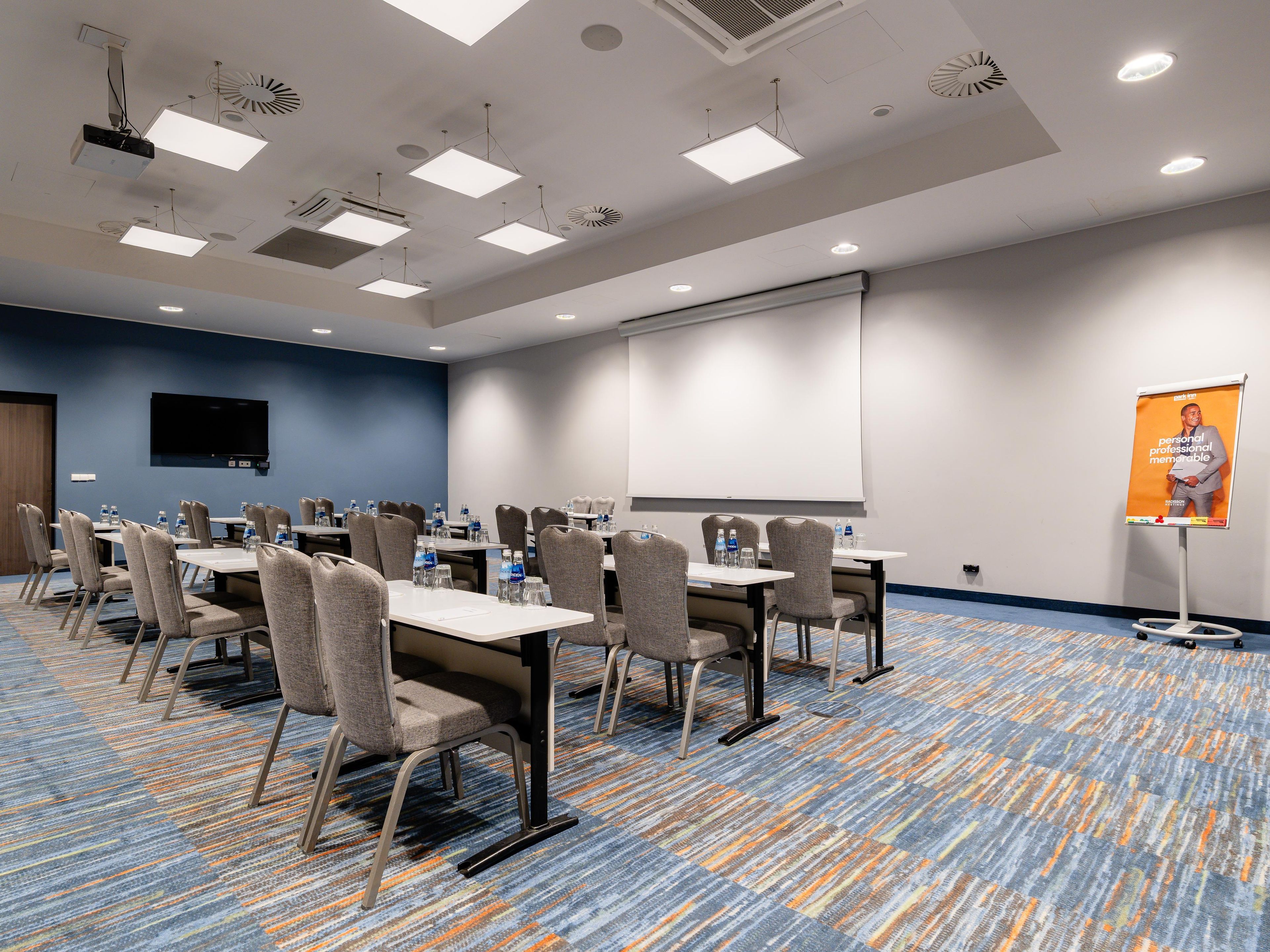 A conference room with tables, chairs, a projector screen, and a presentation screen.