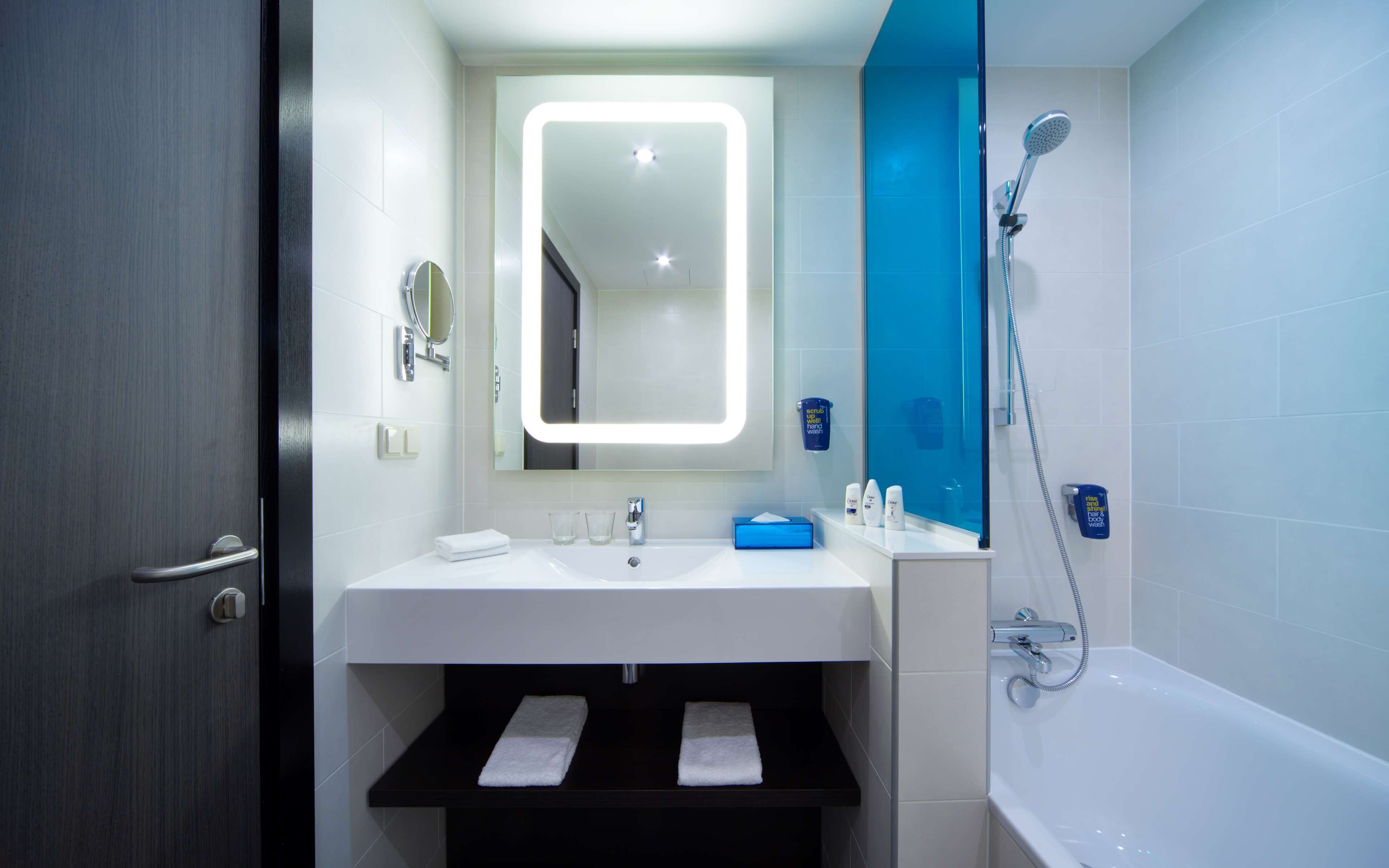 A modern bathroom with a white sink, a mirror with a light, a blue shower wall, and a bathtub.