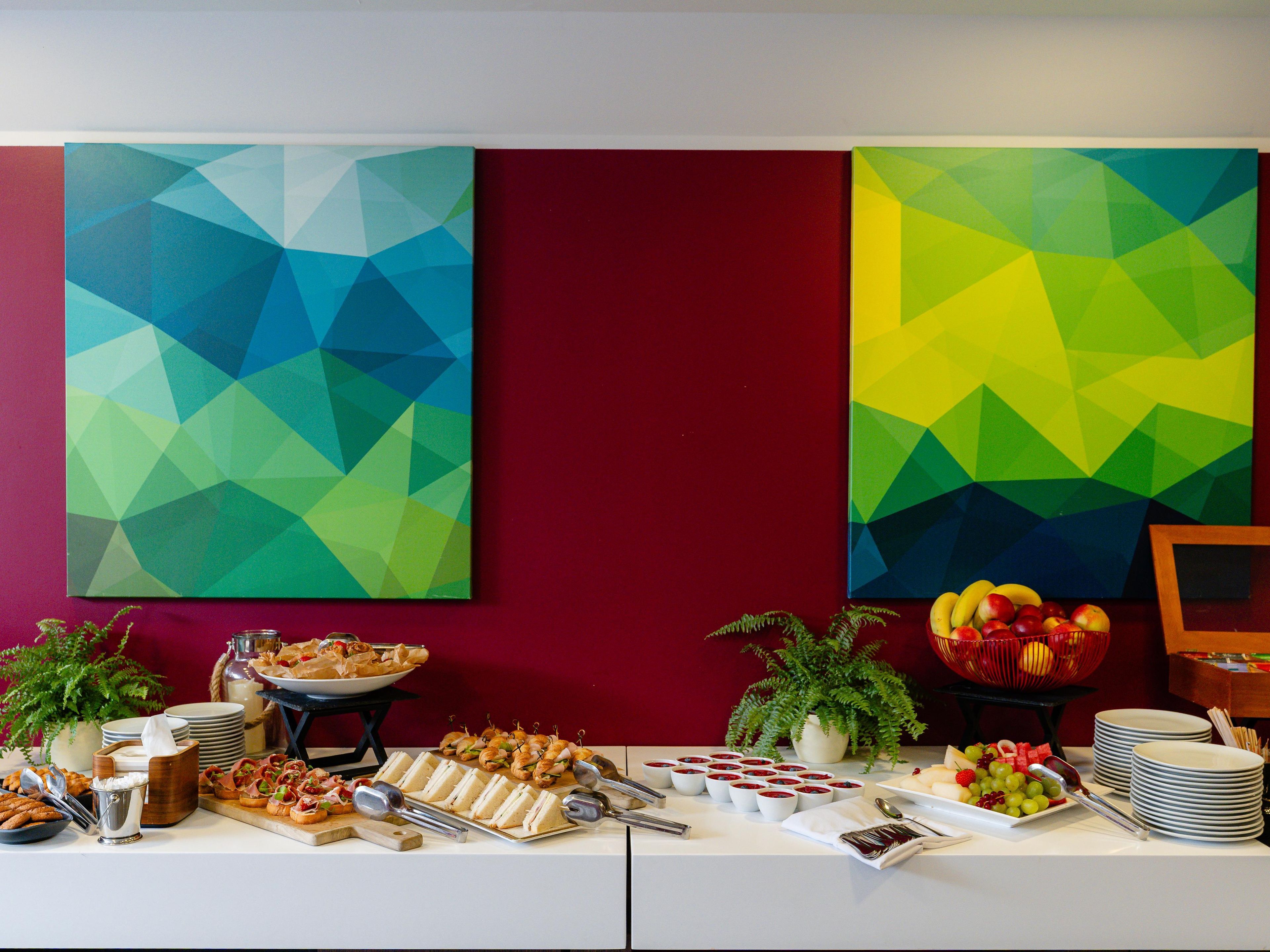 Een buffettafel met diverse gerechten en een rode muur met geometrische schilderijen.