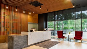 A reception area with a marble counter, red chairs, and large windows offering a view of greenery outside. - Park Inn by Radisson Riga Valdemara (Riga)