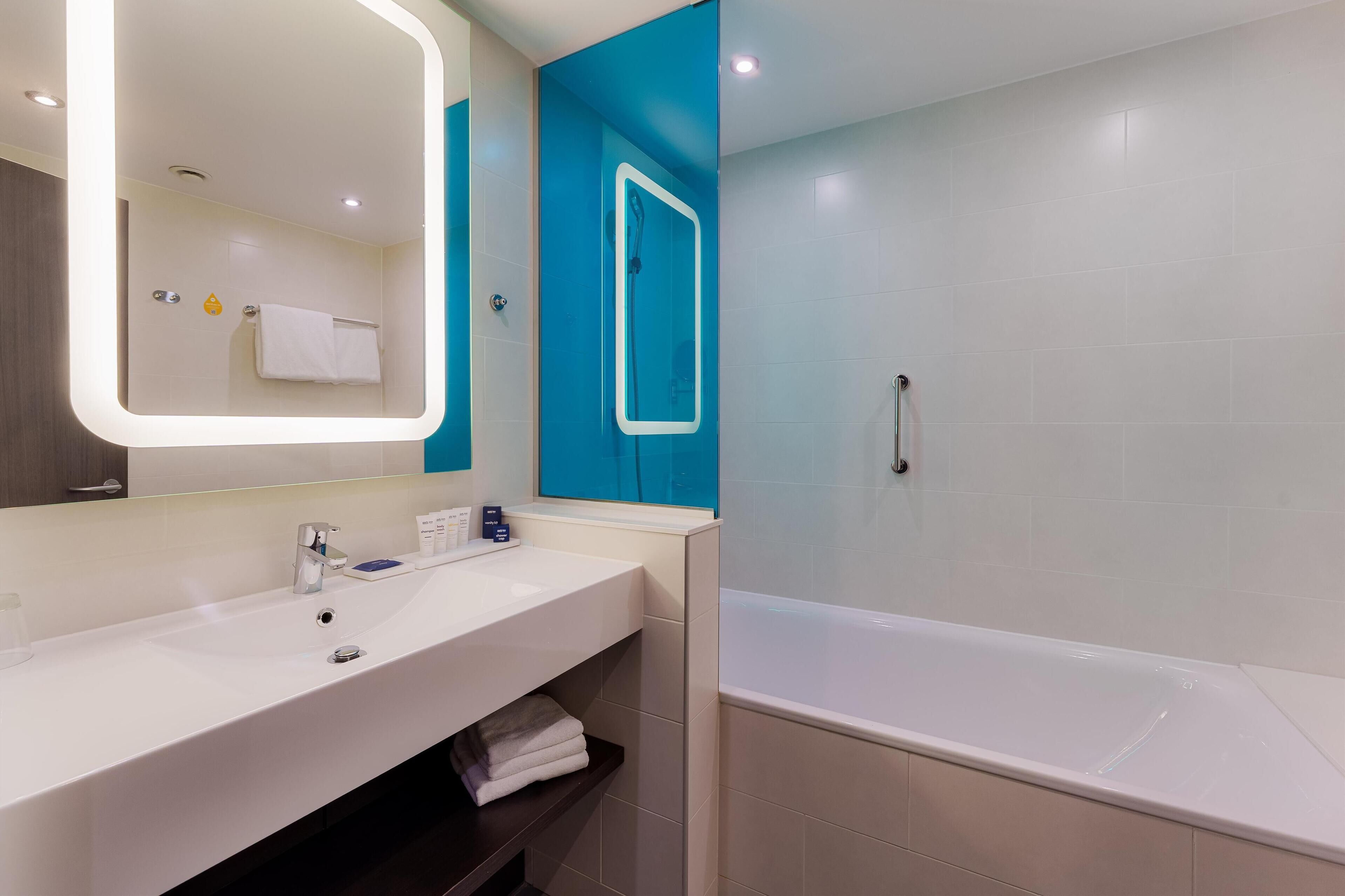 Un baño moderno con un lavabo blanco, un espejo grande y una bañera.