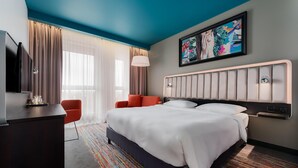 A hotel room with a large bed, a desk, a chair, a TV, and a window with curtains. - Park Inn by Radisson Riga Valdemara (Riga)