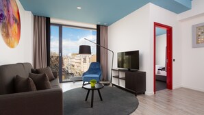 Una sala moderna con un sofá, un sillón azul, un televisor y un ventanal con vistas a la ciudad.