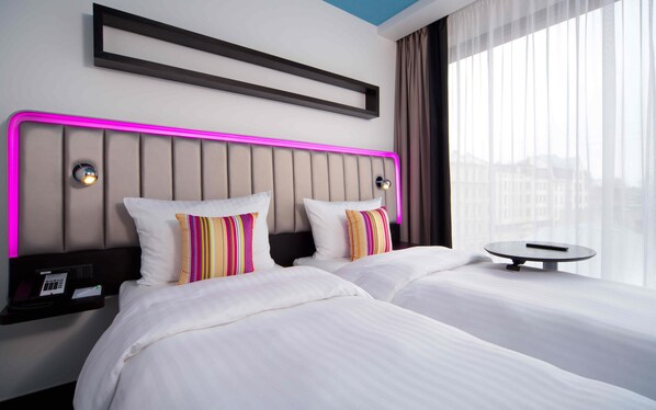 A hotel room with two beds, a bedside table with a phone, and a view of the city through large windows. - Park Inn by Radisson Residence Riga Barona (Riga)