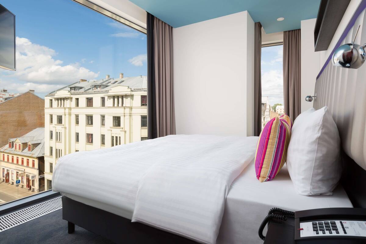 Hotellihuone, jossa on suuri sänky, puhelin sängyn vieressä ja näkymä kaupungin rakennuksiin.