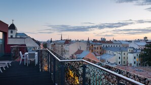 Terraza en la azotea con vistas al paisaje urbano, que incluye varios edificios y la aguja de una iglesia.