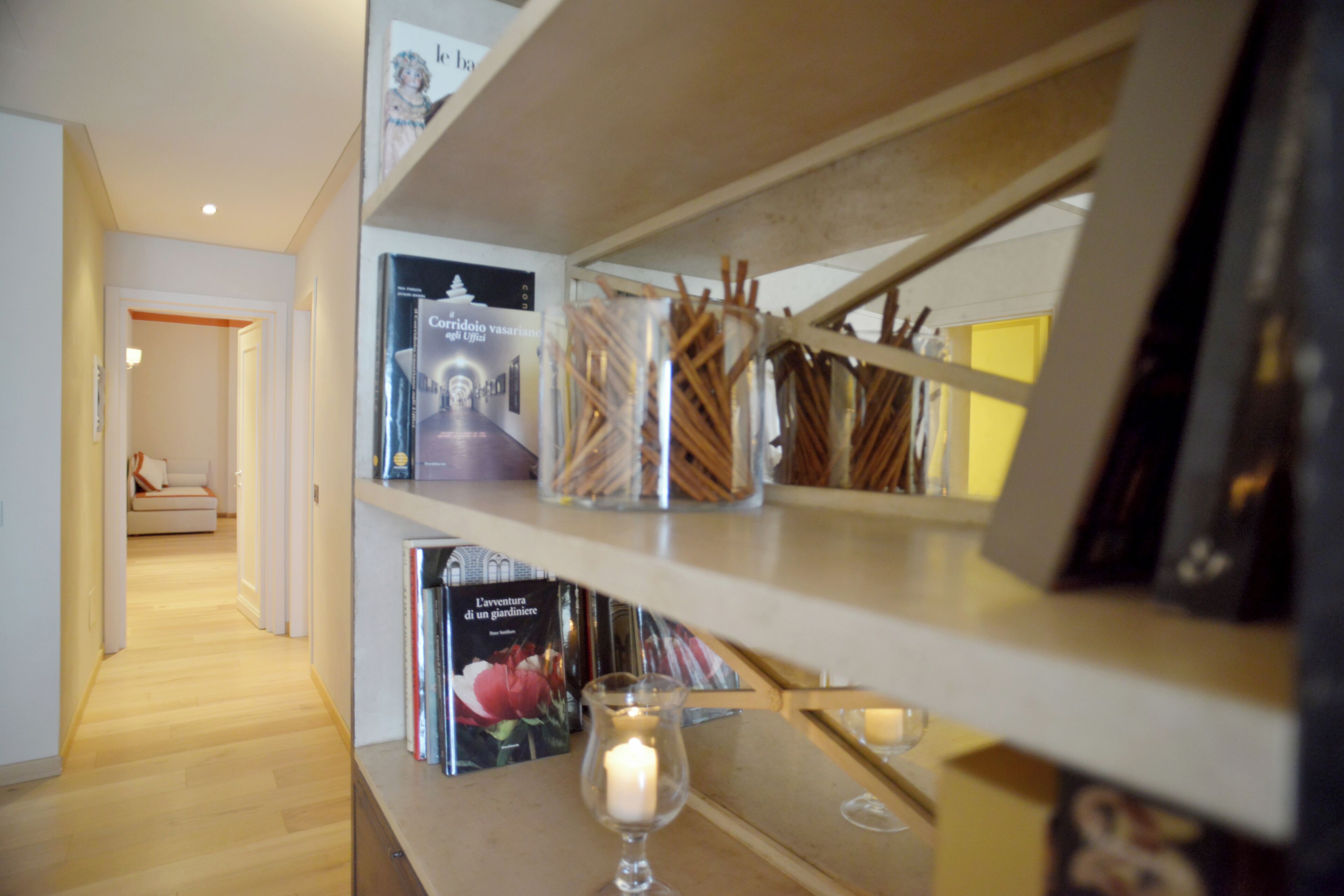 A hallway with wooden flooring, a bookshelf with books and candles, and a framed picture on the wall.
