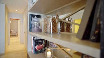 A hallway with wooden flooring, a bookshelf with books and candles, and a framed picture on the wall.