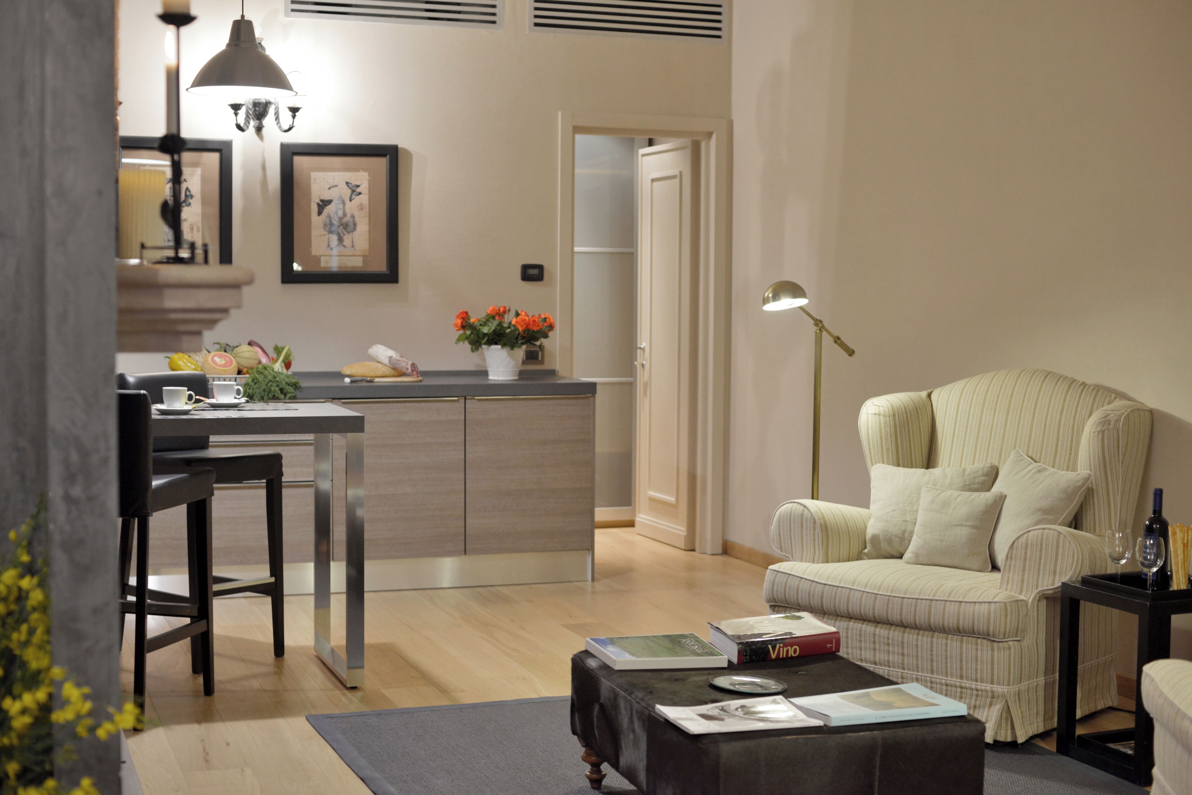 Un salon moderne comprenant un coin repas, un fauteuil à rayures et une petite table sur laquelle sont posés des livres et un verre à vin.