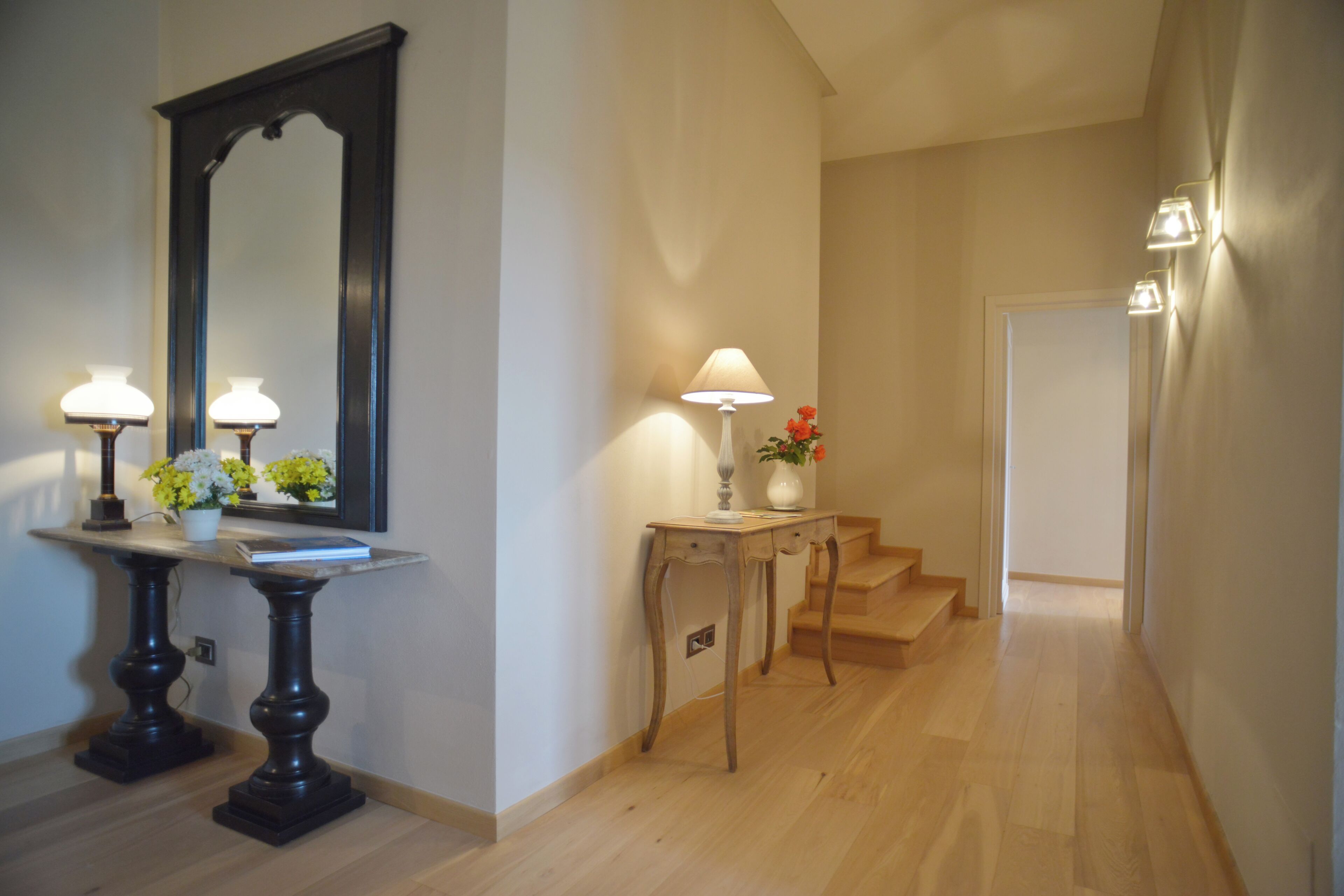 A hallway with a marble table, two lamps, a mirror, and a staircase.