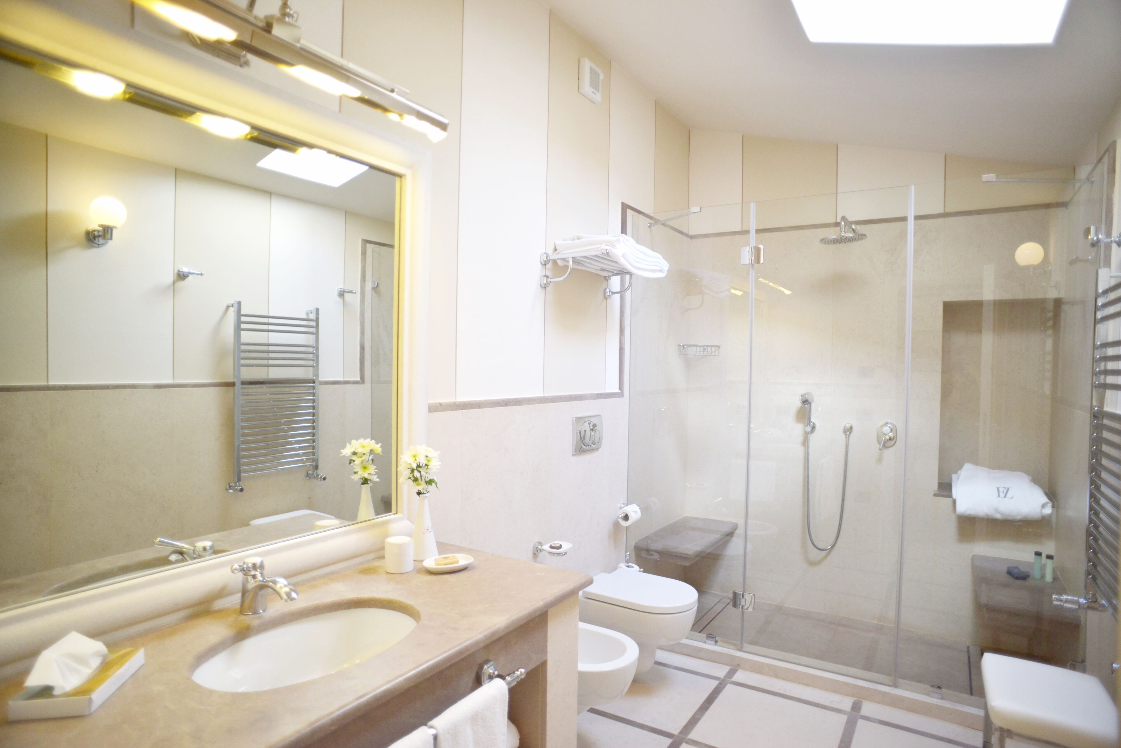 Un baño moderno con un espejo grande, un lavamanos, un inodoro y una zona de ducha con mampara de cristal.