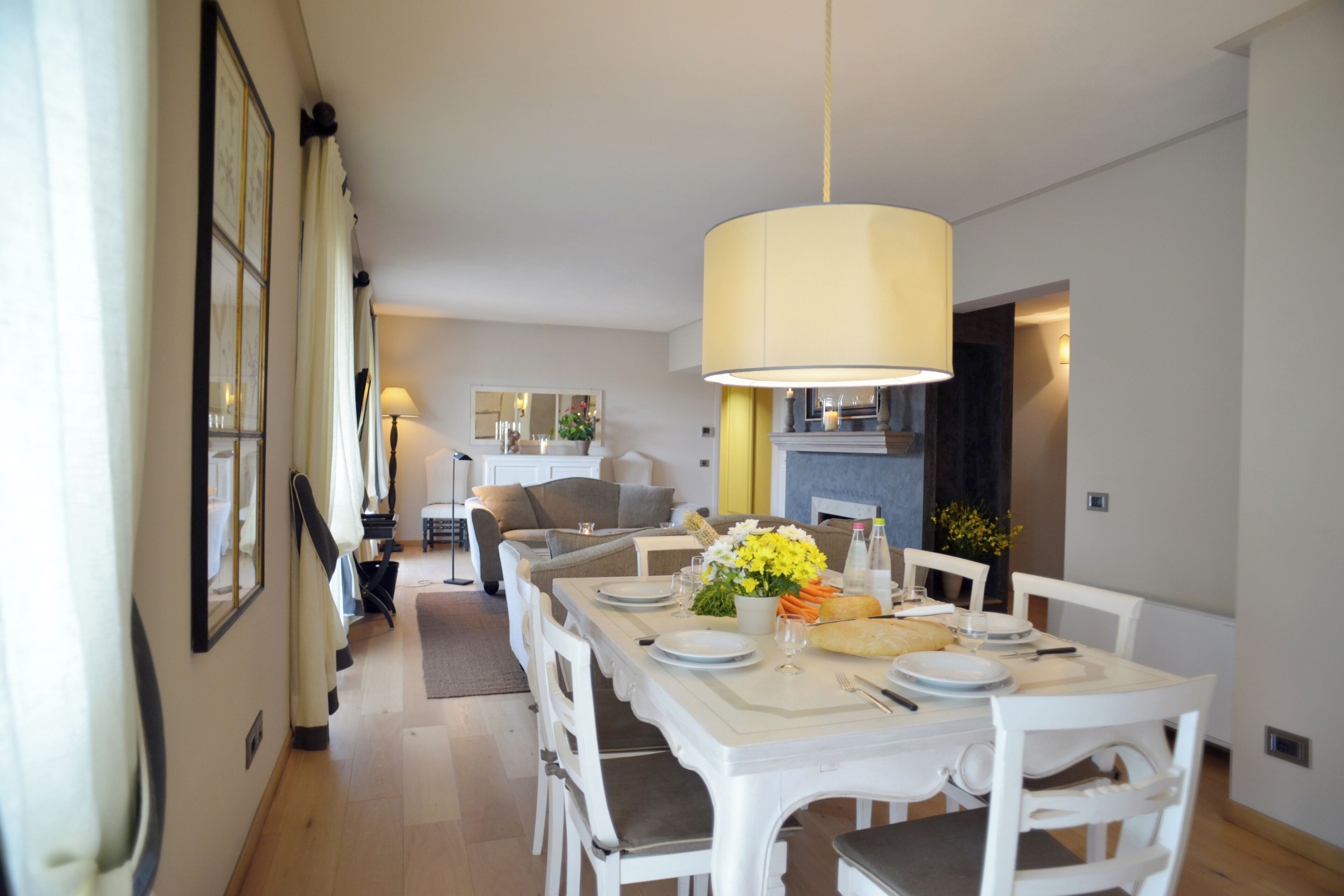 Un coin repas avec une table blanche dressée pour quatre personnes, un luminaire suspendu et une vue sur le salon.