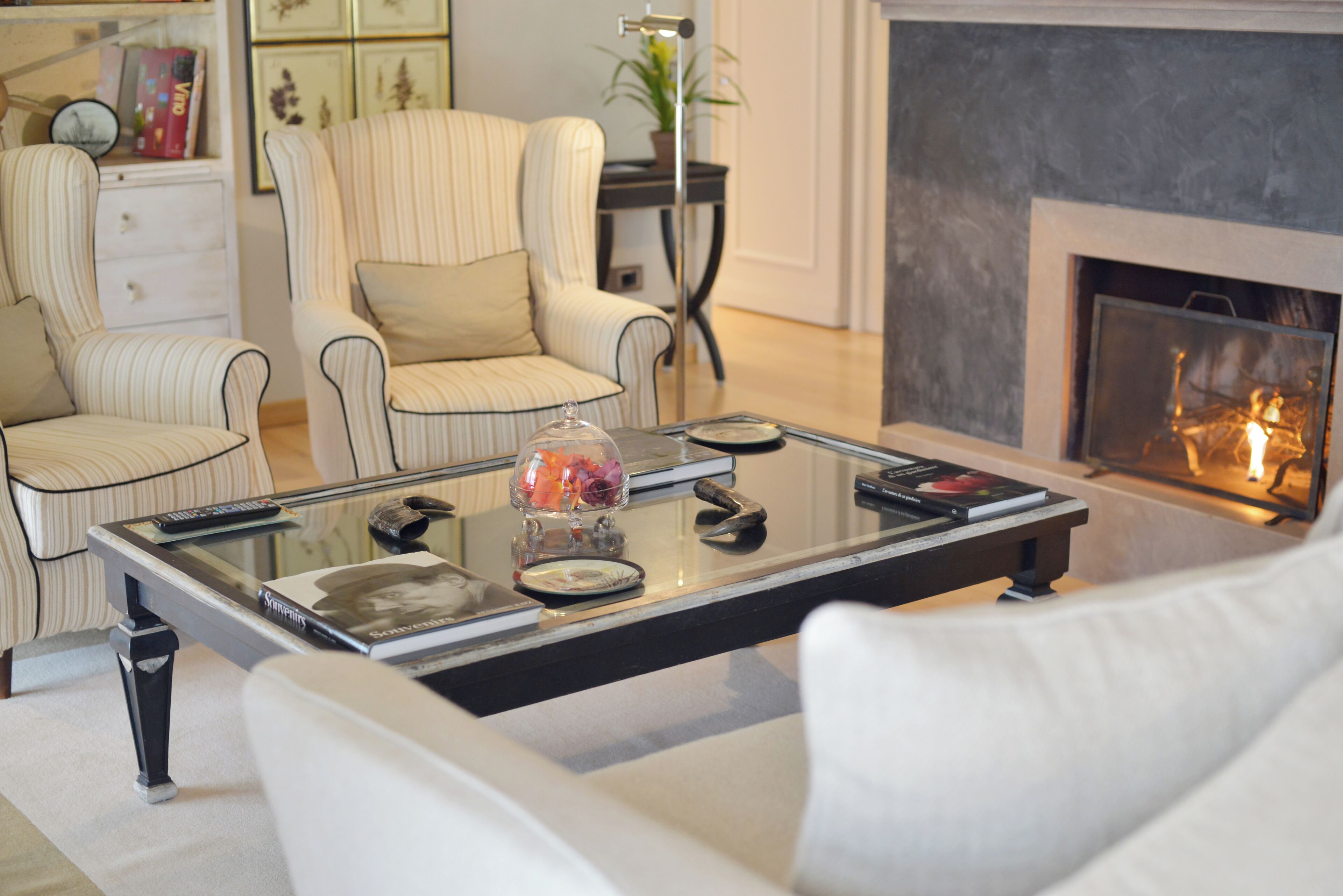 Un salon avec une table basse en verre, des fauteuils à rayures, un canapé blanc et une cheminée.