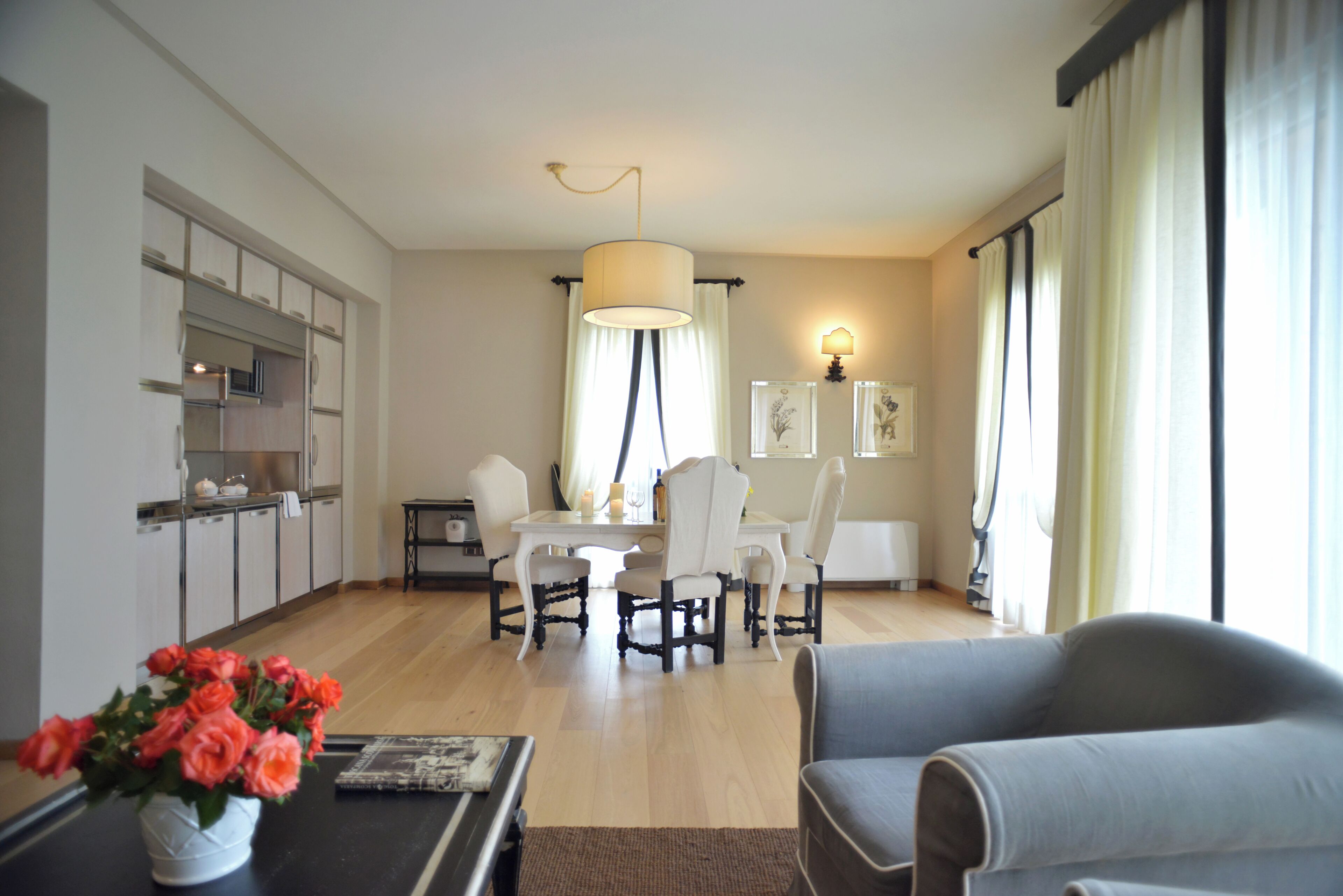 A modern living room with a dining area, a kitchen with cabinets, and a large window with curtains.