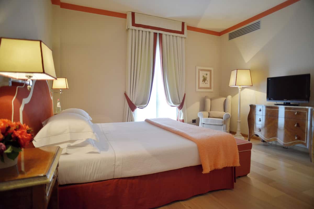 Ein Hotelzimmer mit einem Bett, Nachttischlampen, einem Fernseher, einem Sessel und einem Schminktisch.