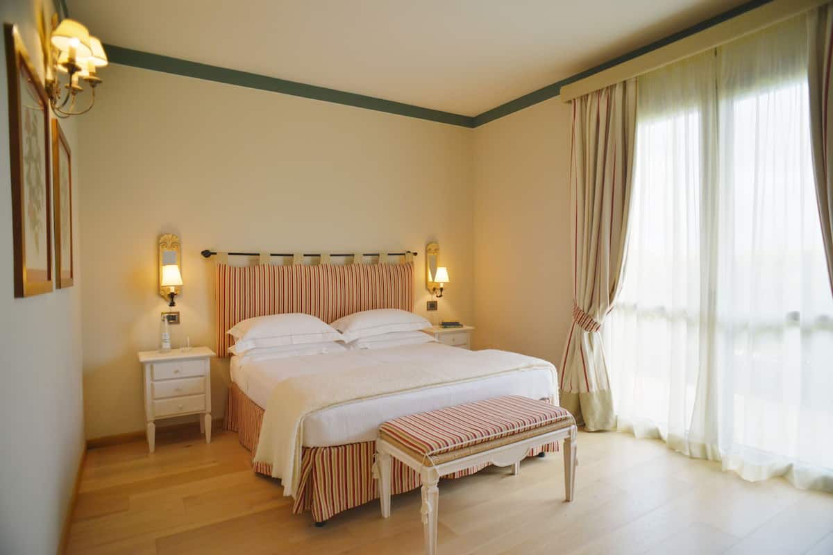 Ein ordentlich eingerichtetes Schlafzimmer mit einem großen Bett, Nachttischen, einer Bank und Vorhängen.