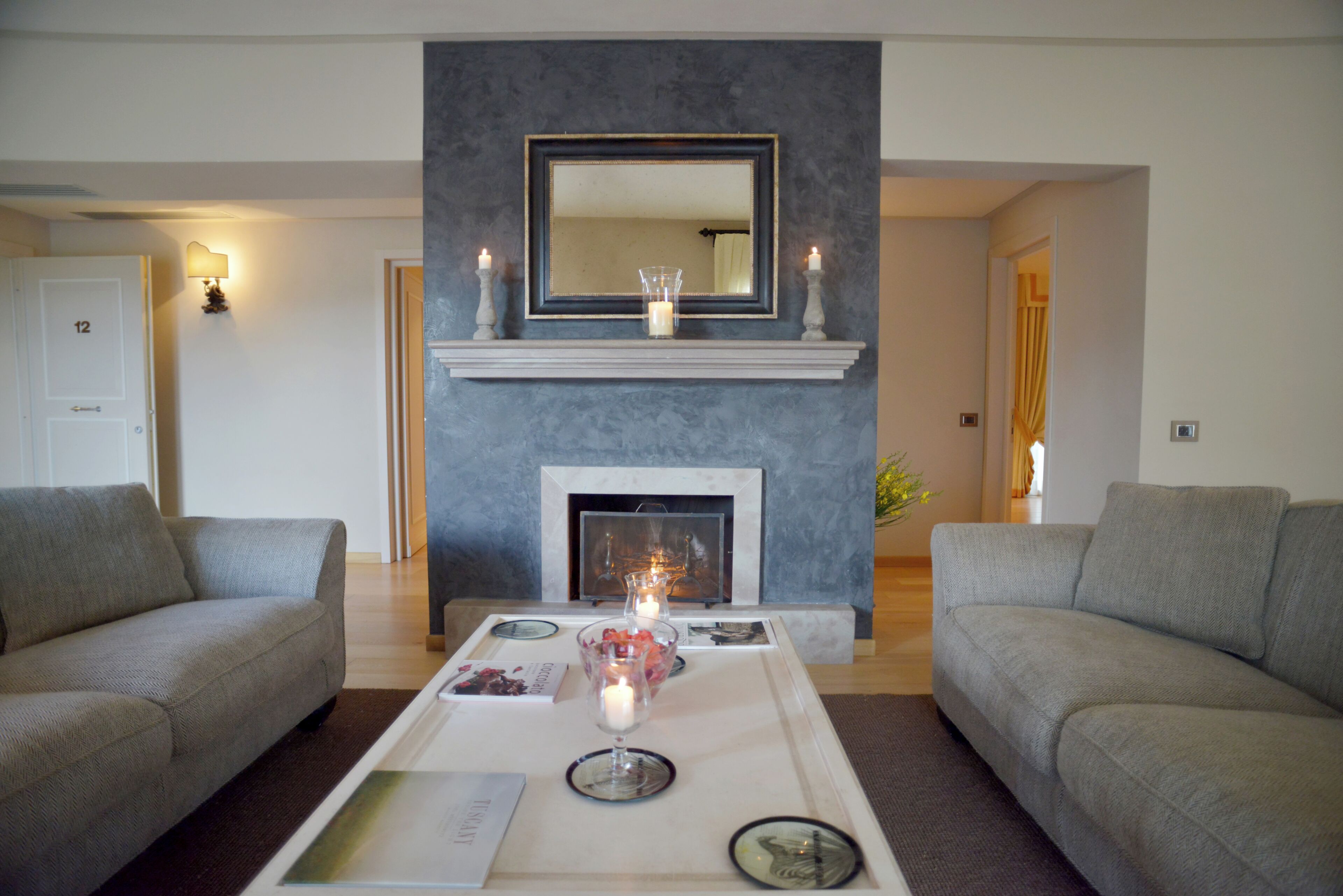 Una sala de estar con chimenea, dos sofás, una mesa de centro con velas y un espejo sobre la chimenea.