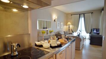 A modern kitchen with a stove, sink, and countertop with various kitchen items. There is a dining area with a sofa and a television.