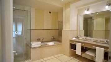 A modern bathroom with a glass shower enclosure, a bathtub, and a vanity with two sinks.