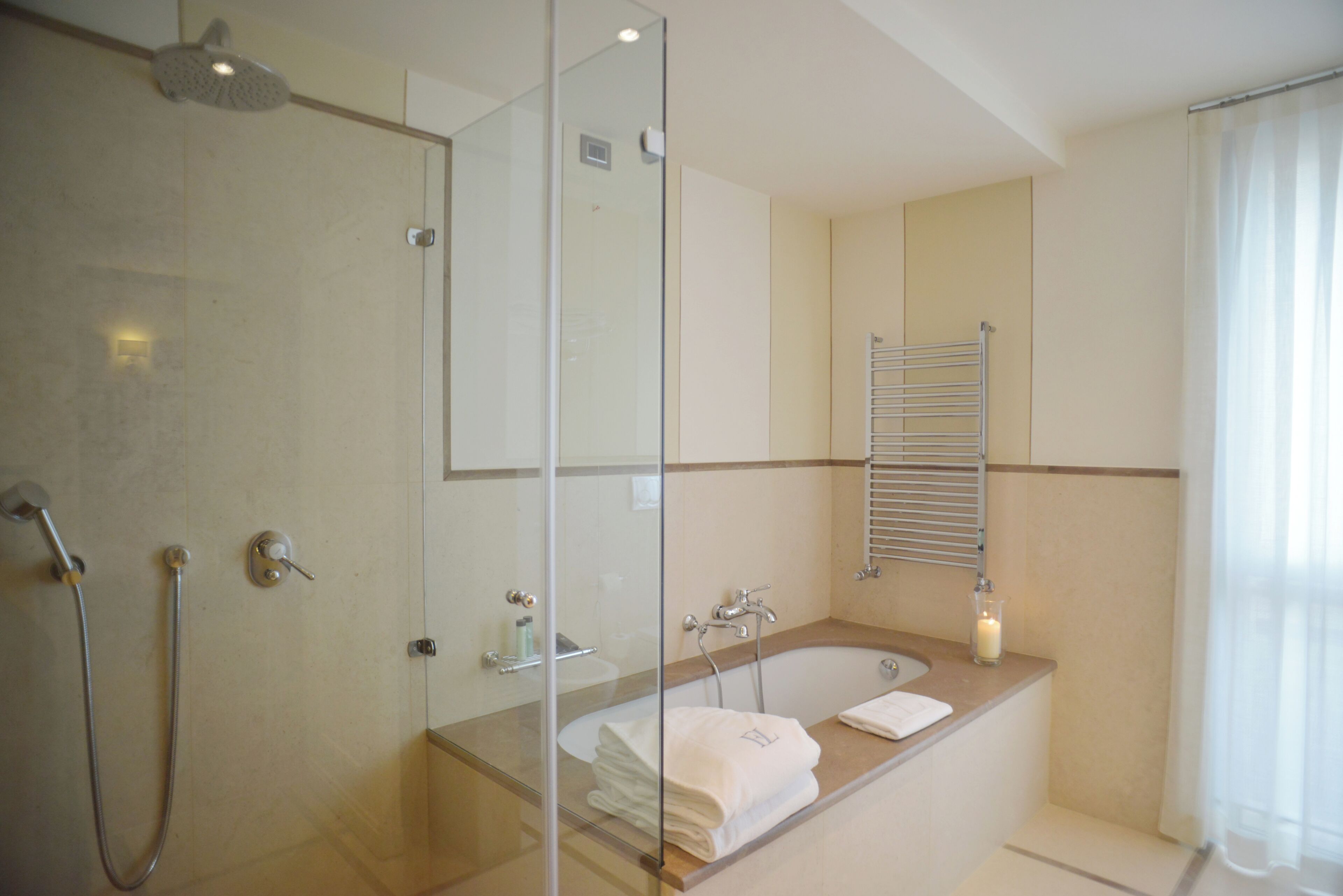 A modern bathroom with a glass shower enclosure, a freestanding bathtub, and a glass-enclosed vanity with a towel rack.