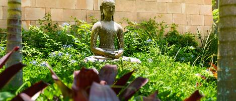 A statue of a seated figure in a garden with a brick wall in the background.