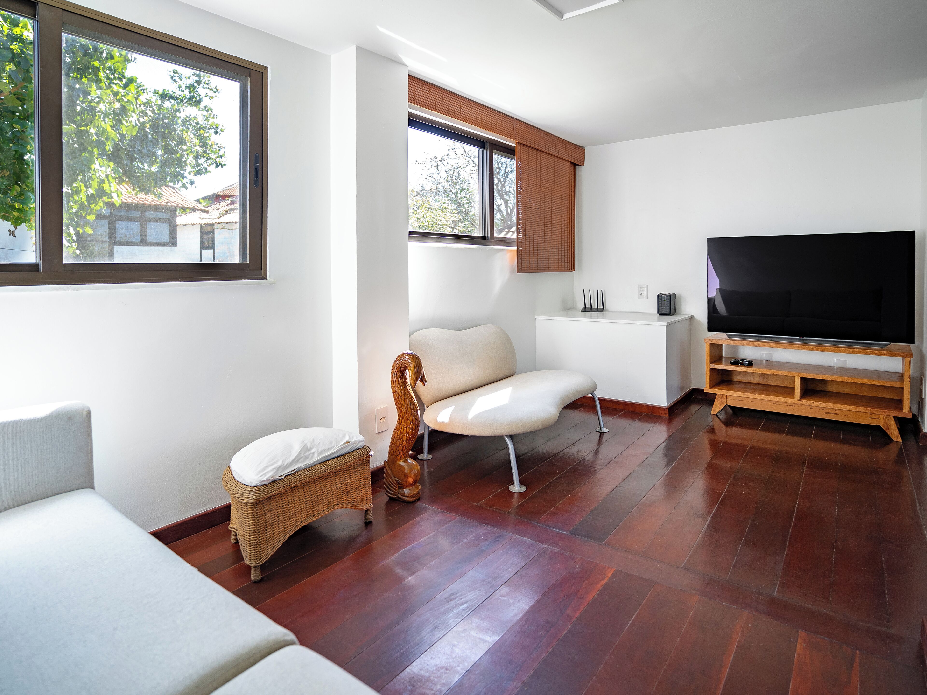 A modern living room with a flat-screen TV, a sofa, a wicker chair, and a wooden entertainment unit.