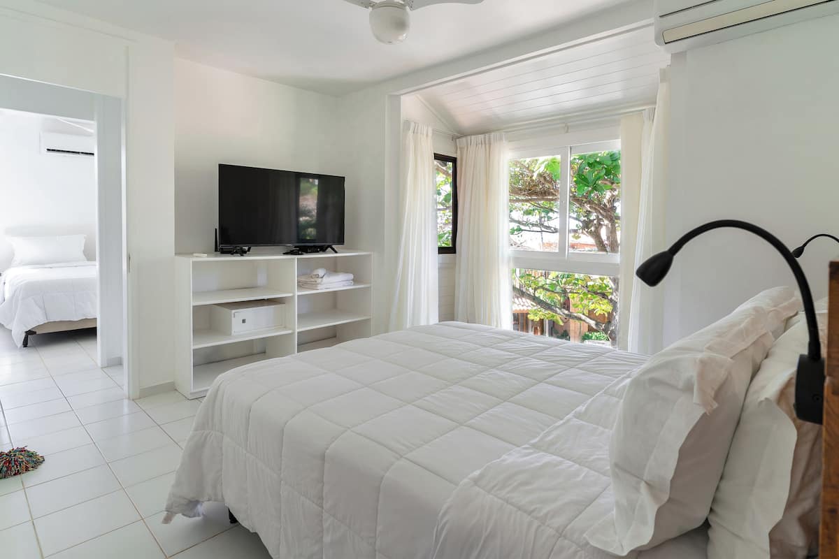 A bedroom with a bed, a TV on a stand, a ceiling fan, and a window with curtains.
