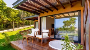 A modern outdoor deck with wooden flooring, white cushioned chairs, and a large glass door leading to a scenic view. - Búzios Espiritualidade Hotel (Búzios)