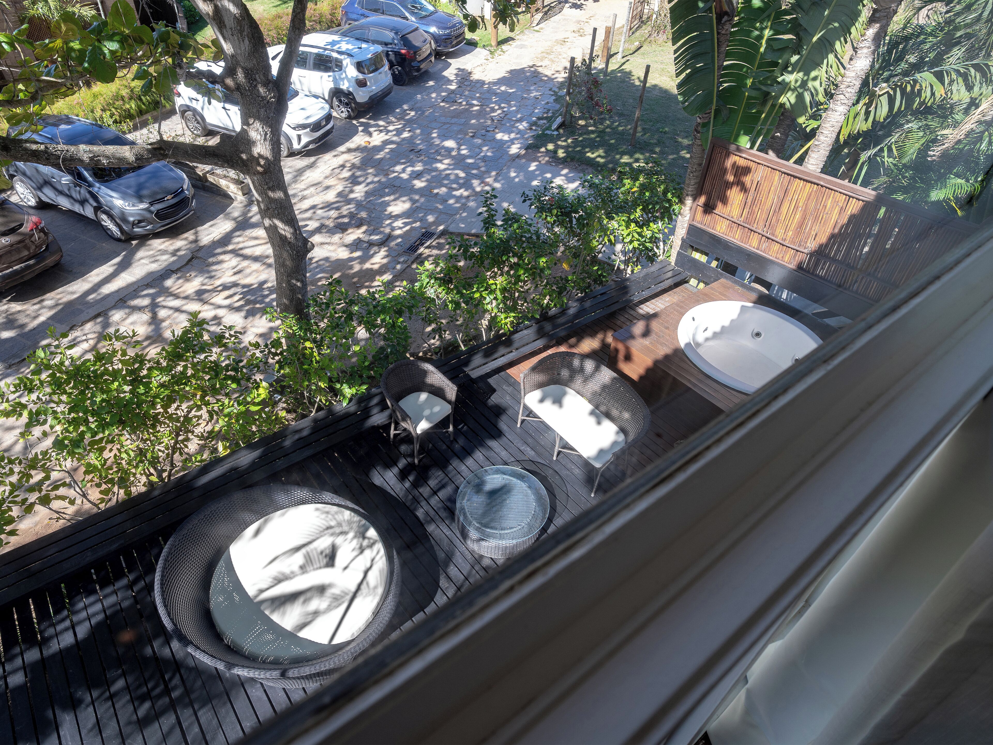A view from a window overlooking a backyard with a wooden deck, two outdoor hot tubs, and a parking area with several cars.