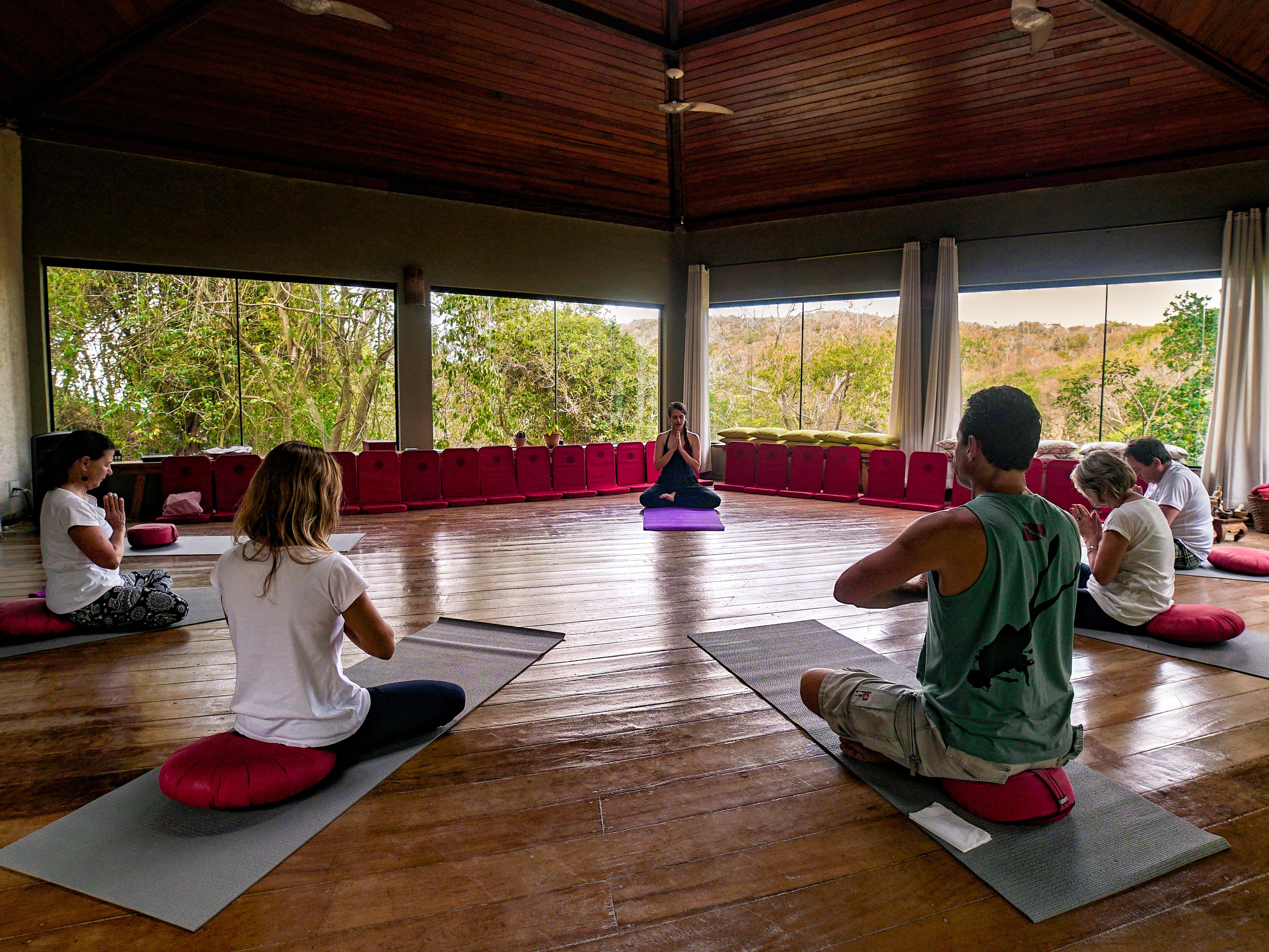 A yoga class in a spacious room with wooden floors and large windows.