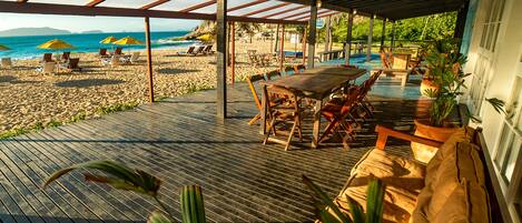 A beachside patio with wooden furniture, umbrellas, and a view of the ocean.