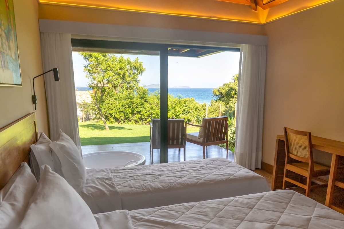A room with two beds, a view of the sea, and a ceiling with a woven pattern.