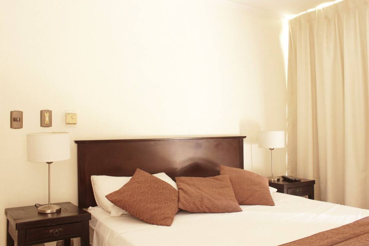 Una habitación de hotel con una cama grande, dos mesitas de noche y una mesita auxiliar.