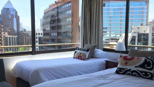 Una habitación de hotel con dos camas, una ventana con vista a la ciudad y una mesita de noche con lámpara.
