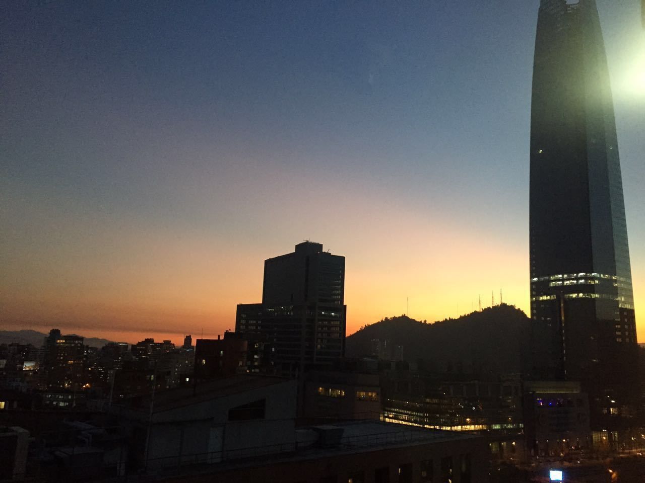 A cityscape at dusk with prominent buildings and a mountain in the background.