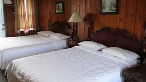 A room with two beds, wooden walls, a window with curtains, and a clock on the wall. - Blue Sky Motel (Gettysburg)