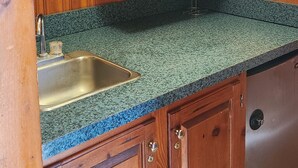 A kitchen with wooden cabinets, a granite countertop, a stainless steel sink, and a microwave. - Blue Sky Motel (Gettysburg)