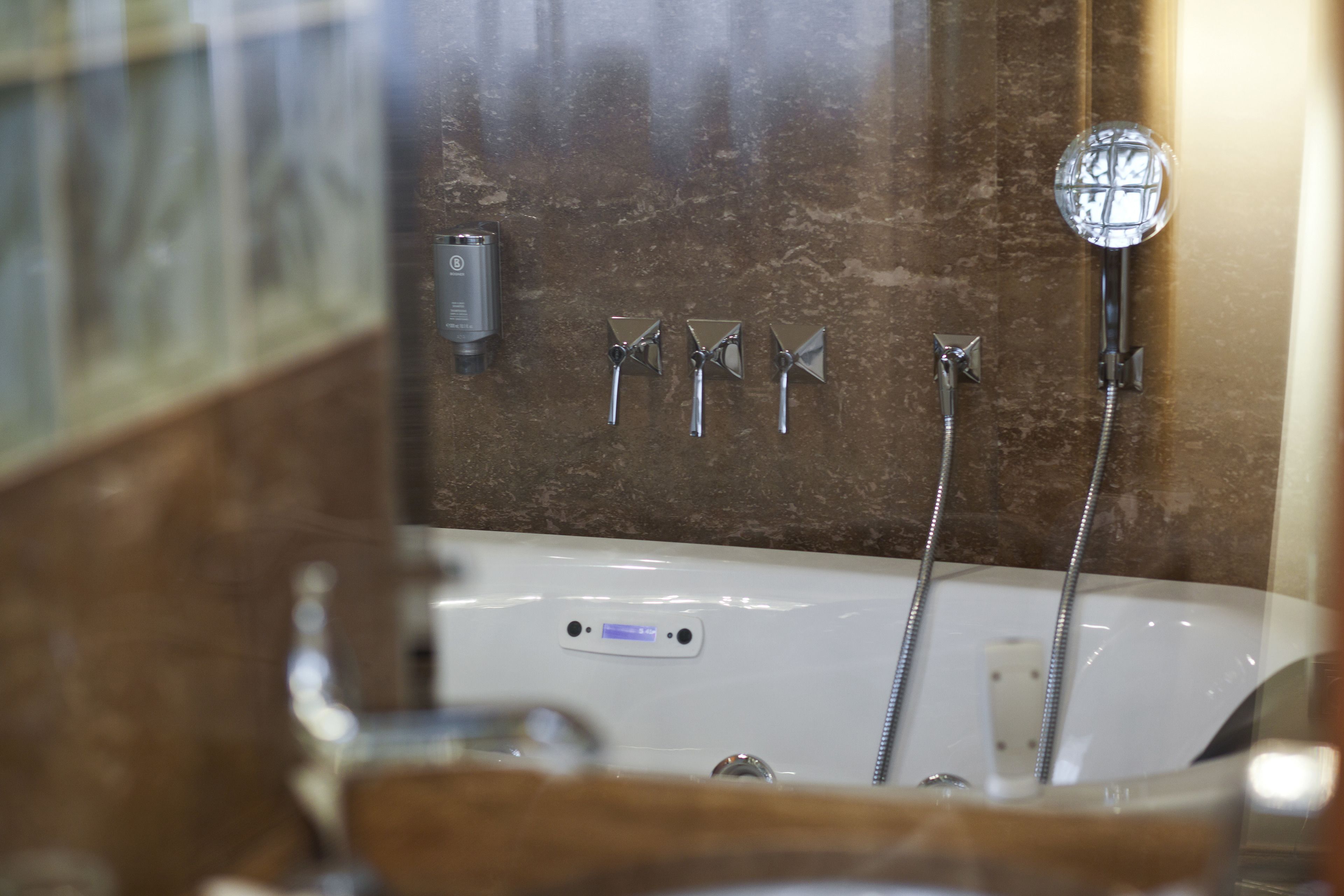 A bathroom with a bathtub, three showerheads, and a glass-enclosed shower.