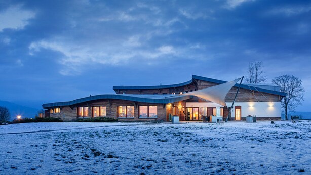 Un edificio moderno de varios pisos con ventanas amplias y un techo curvo, ubicado en un paisaje cubierto de nieve.