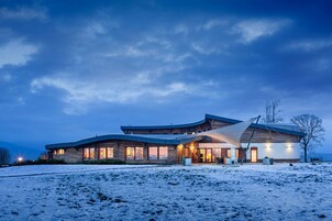 Un edificio moderno de varios pisos con ventanas amplias y un techo curvo, ubicado en un paisaje cubierto de nieve.