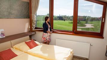 Habitación de hotel con un ventanal grande, una cama con almohadas rojas y amarillas, y vista a un campo de golf.