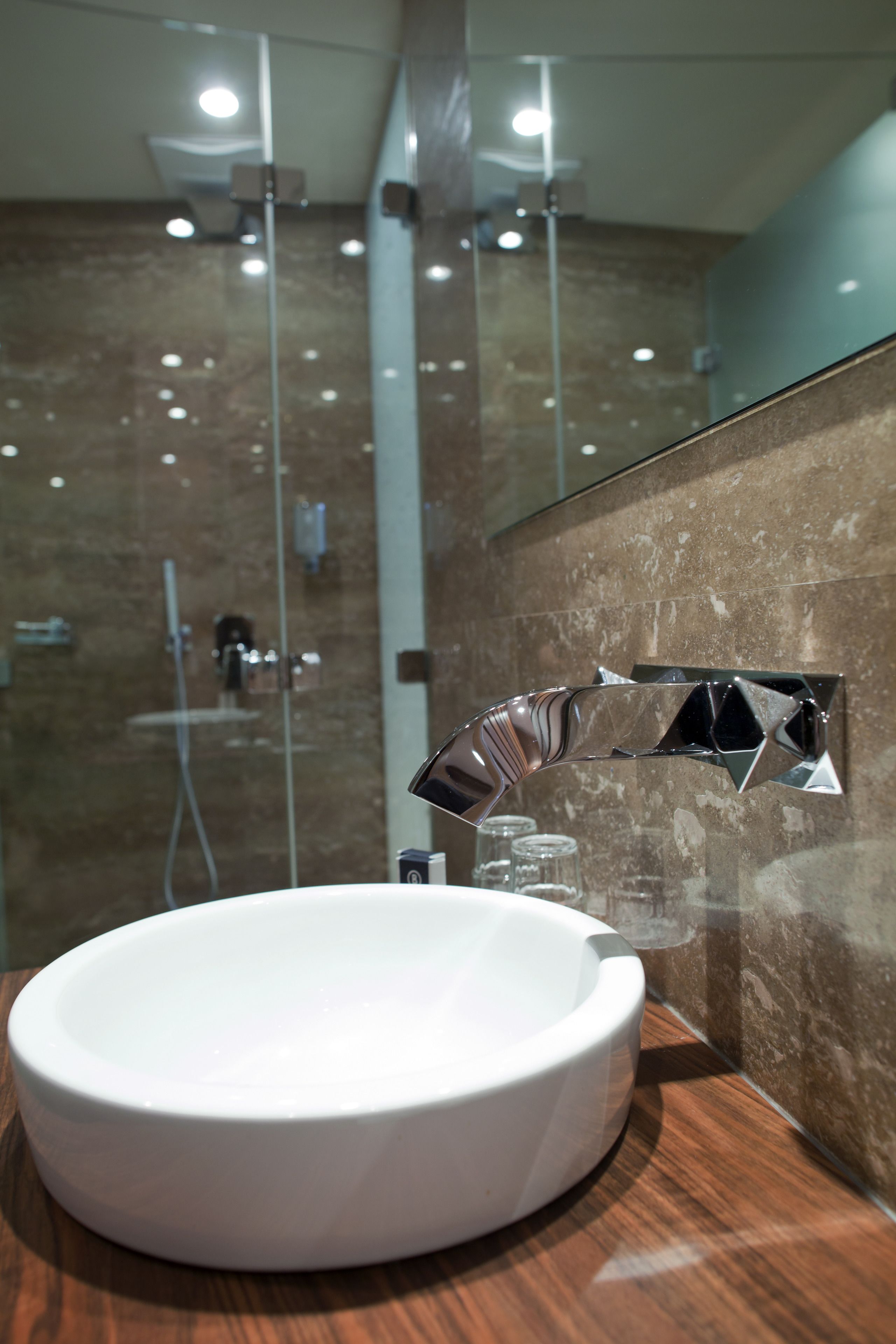 A modern bathroom with a round white sink, a chrome faucet, and a glass shower enclosure.
