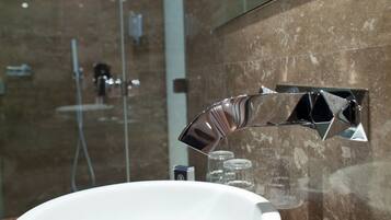 A modern bathroom with a round white sink, a chrome faucet, and a glass shower enclosure.