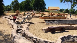 Zona de juegos al aire libre con arena, estructuras de madera y un área de descanso cubierta.