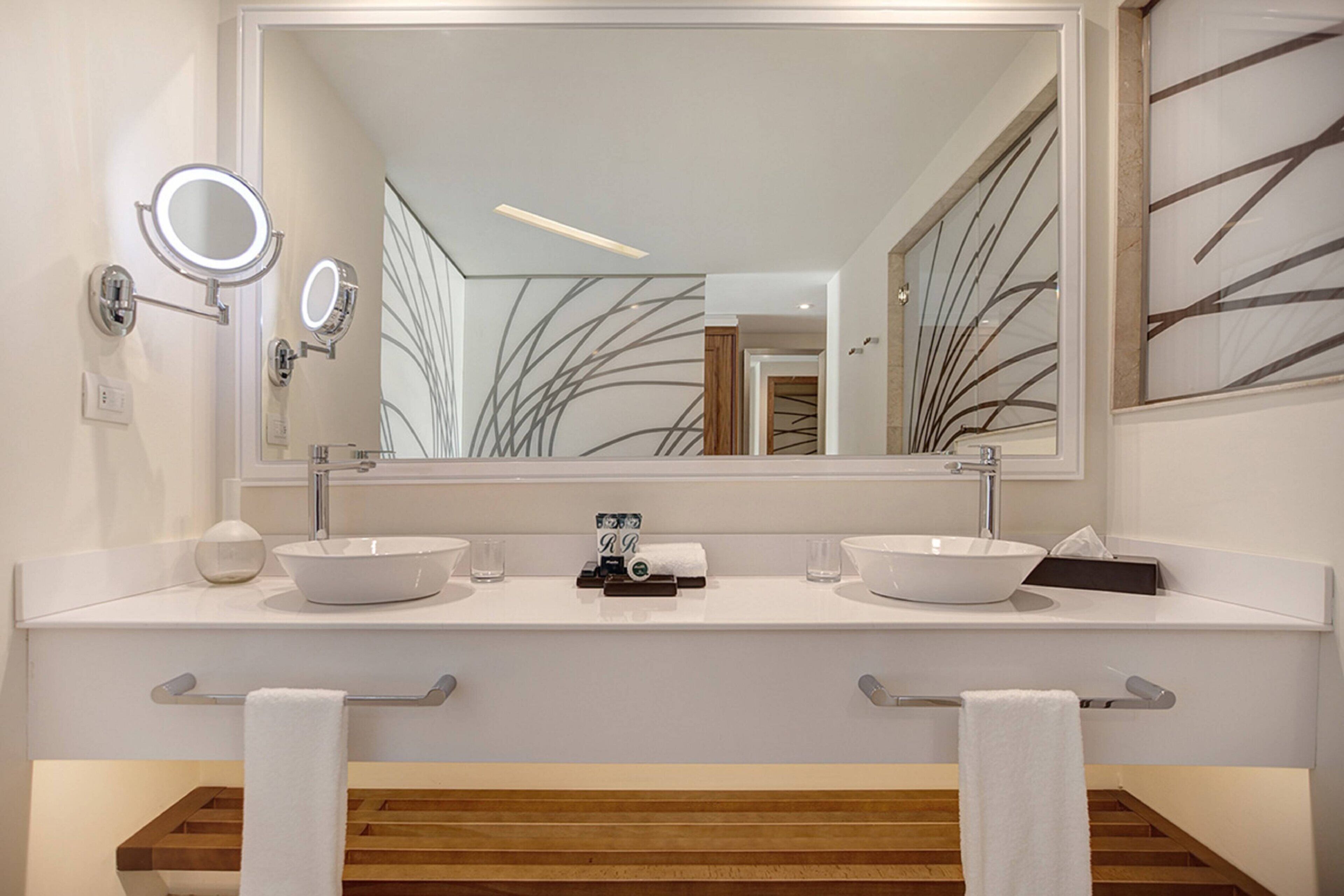 A modern bathroom with two sinks, a large mirror, and a wooden vanity.