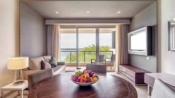 Quarto de hotel moderno com uma mesa de jantar redonda, uma tigela de frutas, um sofá e uma televisão.