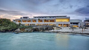 Un hotel moderno con varios pisos, grandes ventanales y vista a una masa de agua tranquila.