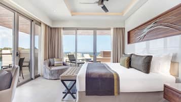 A modern hotel room with a large bed, a ceiling fan, a balcony with seating, and a view of the sea.