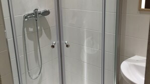A glass-enclosed shower stall with a white tiled wall, a white sink, and a mirror above the sink. - Malta Rent Rooms (Gzira)